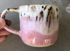 a hand holding a pink and white coffee mug with black streaks on it's side