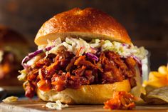 a pulled pork sandwich with coleslaw on a cutting board next to potato chips