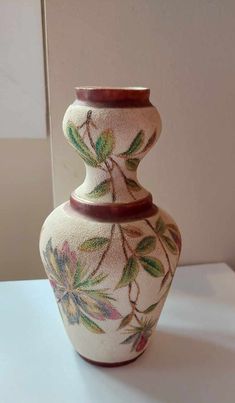 a white vase sitting on top of a table with flowers painted on the side of it