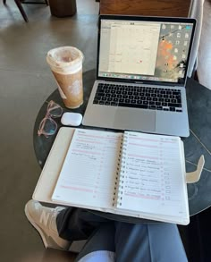 a laptop computer sitting on top of a table next to a notebook and cup of coffee