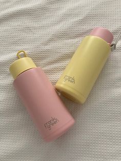 two pink and yellow water bottles sitting on top of a white bed sheet next to each other