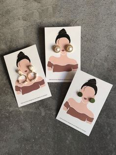 three postcards with earrings on them sitting next to each other in front of a concrete floor