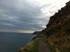 a path going up the side of a cliff by the ocean under a cloudy sky