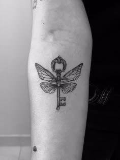 a black and white photo of a dragonfly with a key tattoo on the arm