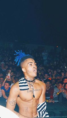 a shirtless man with blue hair standing in front of an audience at a concert