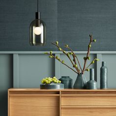 a wooden dresser topped with vases filled with flowers and greenery next to a gray wall