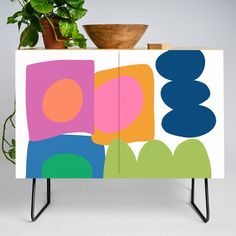 a cabinet with an abstract design painted on the front and sides, sitting next to a potted plant