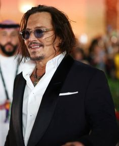 a man in a tuxedo and sunglasses standing next to another man with long hair