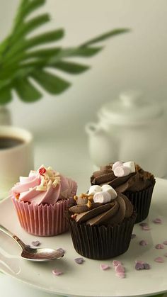 three cupcakes are sitting on a plate next to a coffee mug and spoon