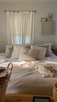 a bed with white sheets and pillows in a bedroom next to a basket on the floor