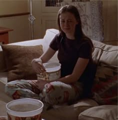 a woman sitting on a couch with two buckets of popcorn