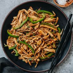 a black plate topped with noodles and green peppers next to chopsticks on a table