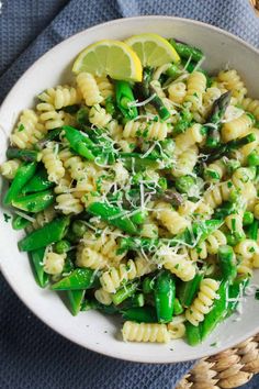 a white bowl filled with pasta and vegetables on top of a blue towel next to a lemon wedge