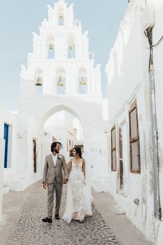 a bride and groom walking down an alley way in front of a white building with arched doorways