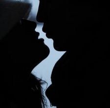 two people are silhouetted against a window with their heads turned to the side, one is kissing the other