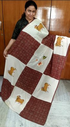 a woman is holding up a red and white blanket with cartoon cats on it in front of wooden cabinets