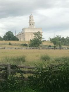 a large white building sitting on top of a lush green field next to a wooden fence