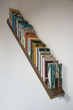 the books are lined up on the wall by the stair case, which is made out of wooden planks