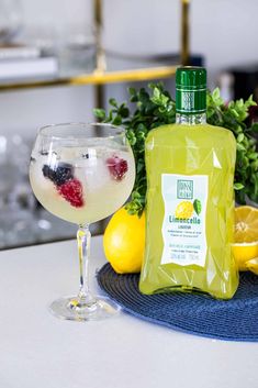 a bottle of lemonade next to a glass filled with liquid and fruit on the table