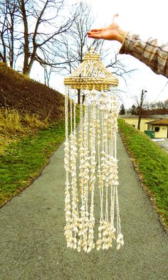 a hand is holding a chandelier on the side of a path in front of some trees