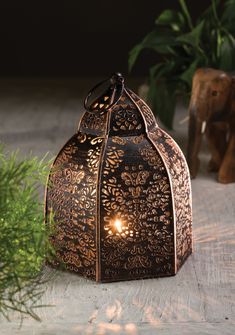 an intricately designed lantern is lit up on the table next to some potted plants