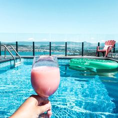 a person holding up a drink in front of a swimming pool with an ocean view