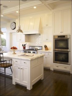 a large kitchen with white cabinets and an island in the middle, along with a clock on the wall