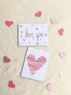 two valentine's day cards with hearts scattered around them on a white blanket and pink polka doted paper