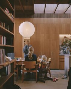 three children sitting at a table in a room with bookshelves and wooden shelves