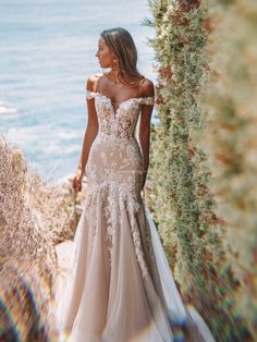 a woman in a wedding dress standing on the side of a cliff by the ocean