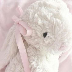 a white stuffed animal with a pink ribbon around its neck on a light pink blanket