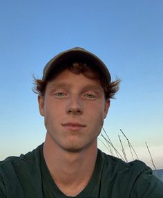 a young man wearing a hat and looking at the camera with blue sky in background