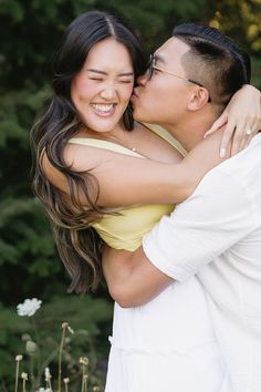 a man and woman kissing each other in front of some flowers with trees behind them