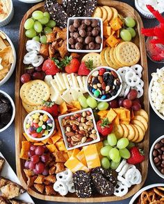 a wooden platter filled with cheese, crackers, nuts and fruit on top of a table