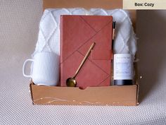 an open box containing a notepad, pen and coffee mug with the contents in it