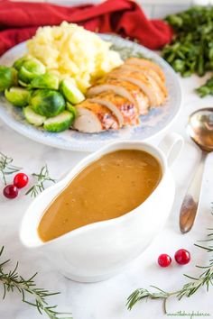 a white bowl filled with gravy next to a plate of vegetables and meat