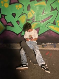 a young man sitting on the ground with his skateboard in front of graffiti covered wall