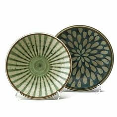 two green and white plates sitting next to each other on top of metal stands in front of a white background