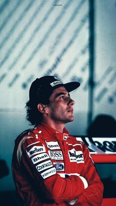 a man sitting in front of a red table wearing a racing suit and black hat