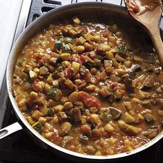 a pan filled with food sitting on top of a stove next to a wooden spoon