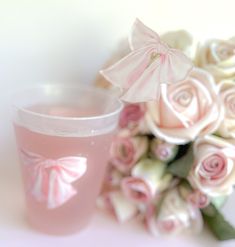 a bouquet of roses next to a plastic cup with pink liquid in it on a white surface