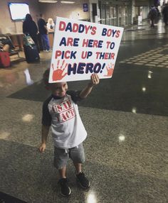 a young boy holding up a sign that says daddy's boys are here to pick up their hero