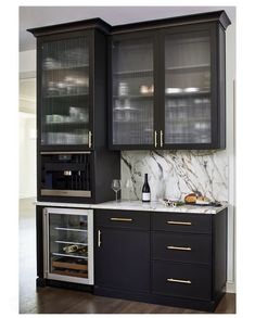 a kitchen with black cabinets and marble counter tops, wine glasses on the bottom shelf