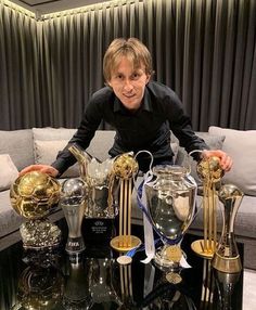 a man sitting on top of a couch next to many trophies in front of him