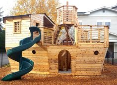 a wooden pirate ship playset with a slide in the front and a house behind it