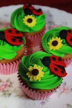 four cupcakes decorated with green frosting and ladybug decorations on a plate