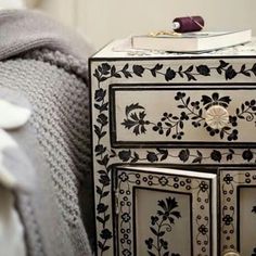 a black and white dresser with flowers painted on it's drawers next to a bed