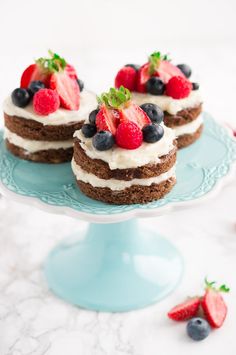 three small cakes with strawberries and blueberries on top sit on a cake plate