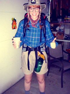 a woman wearing a cowboy hat and holding a coffee cup in her hand while standing next to a wall