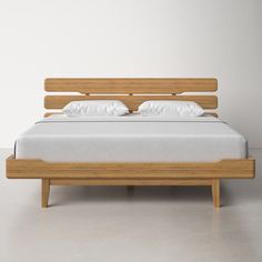 a wooden bed with white sheets and pillows on top of the headboard, in front of a plain wall